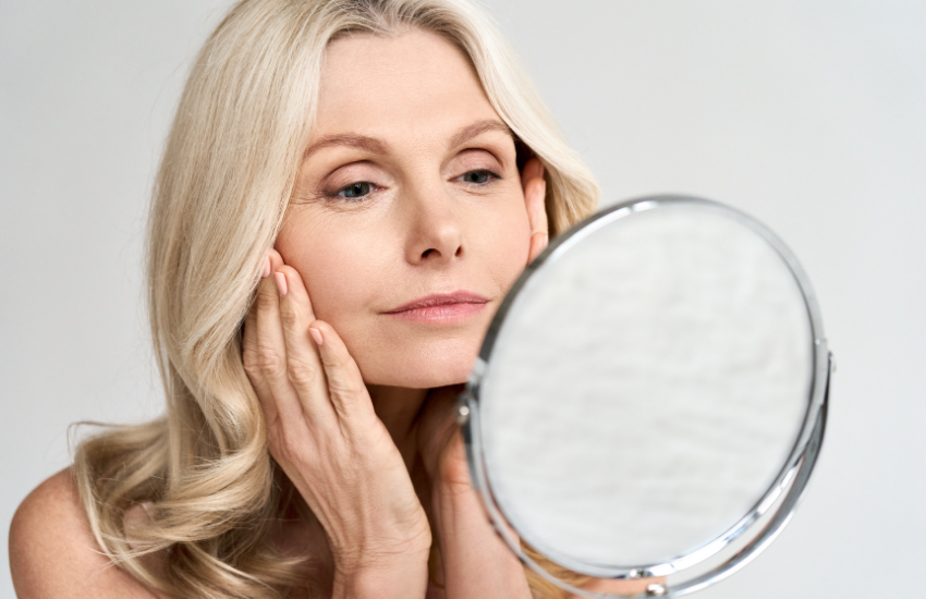 Woman looking into mirror, holding her face in relation to Complete Skin Needling.